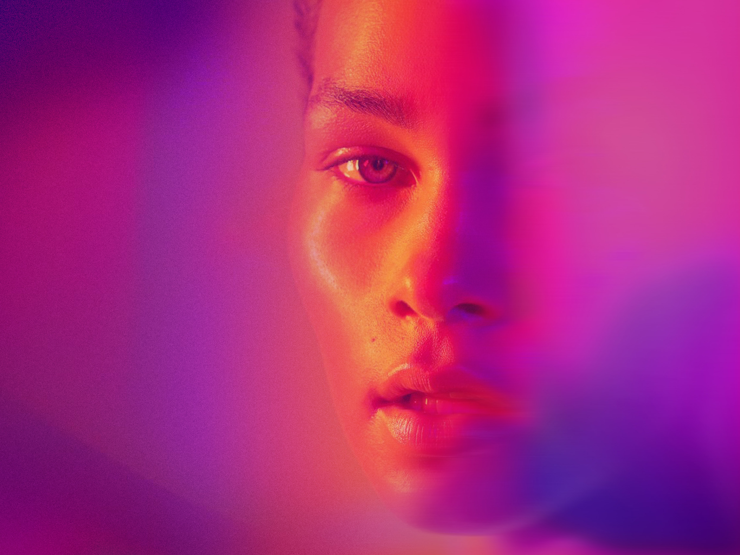Close-up portrait of a woman’s face illuminated by pink and purple neon light