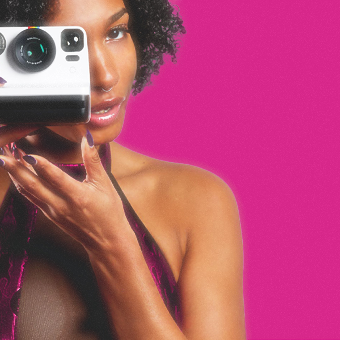 Close-up mirror selfie of a woman with curly hair against a vivid pink background